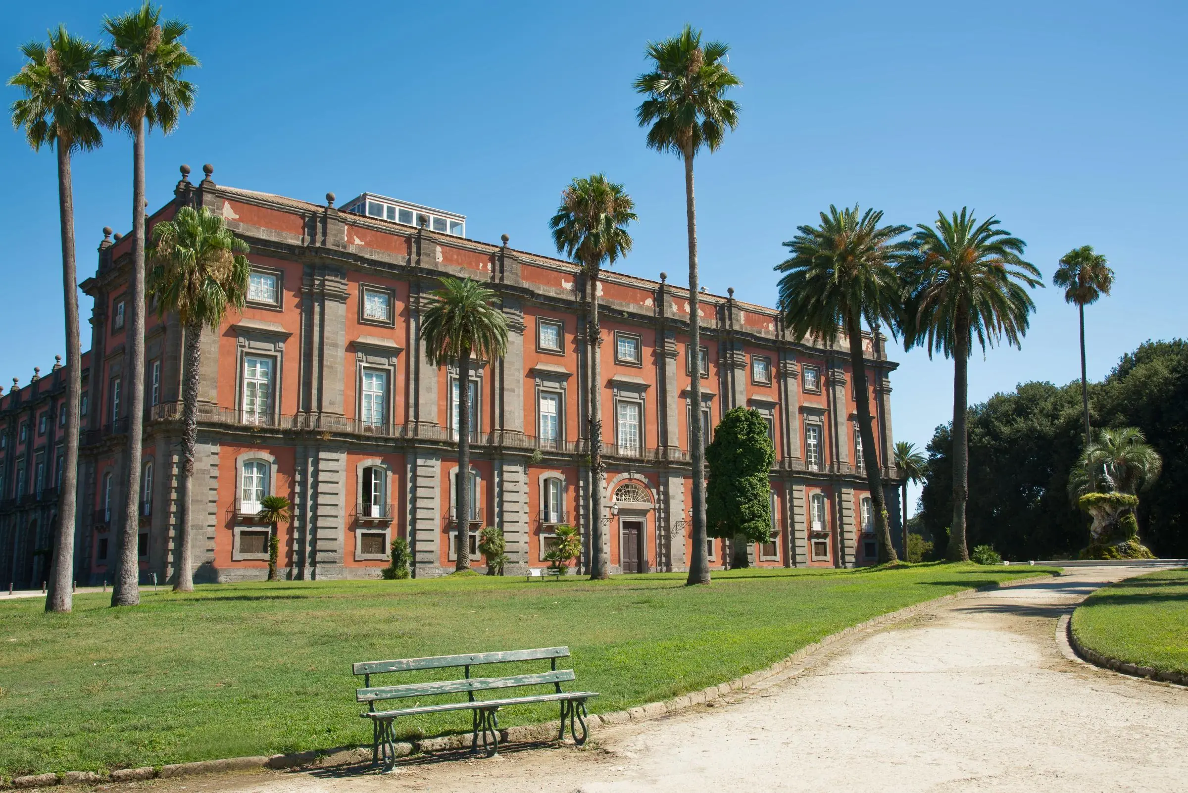 The red facade of the Capodimonte Museum surrounded by green parkland in Naples