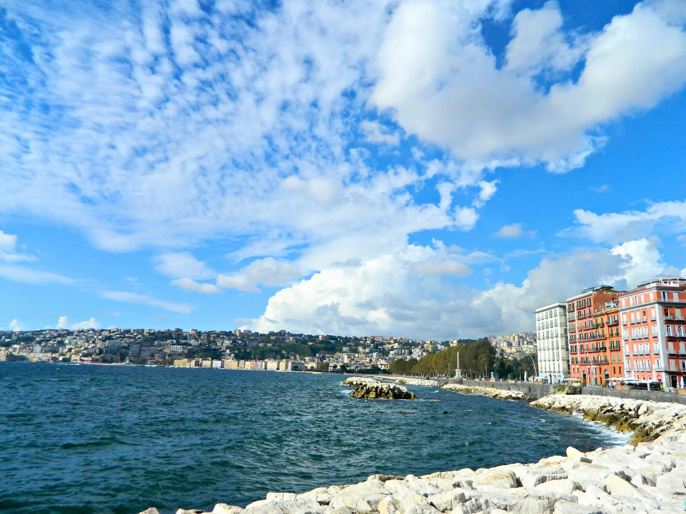 People walking along the Lungomare promenade in Naples with Mount Vesuvius in the background